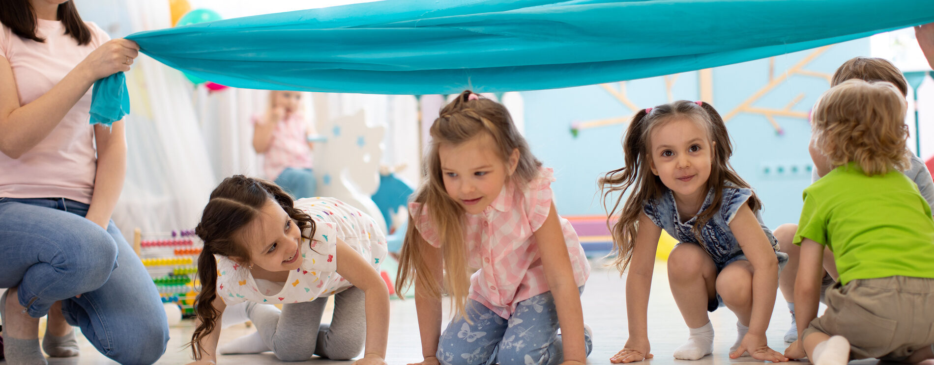 jeunes enfants en train de jouer sous une bâche bleur tenue par des adultes