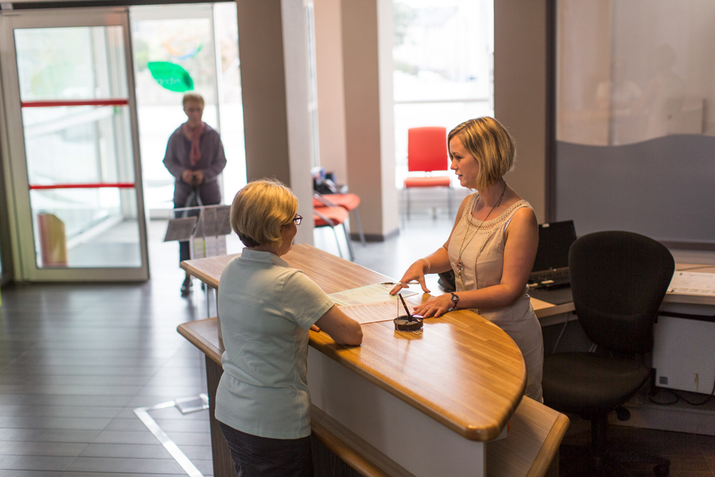 jeune femme blonde à l'accueil d'une mairie qui reçoit une personne en demande d'informations