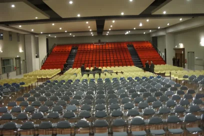 Salle de spectacle vide avec des fauteuils rouges et des chaises grises. La pièce est éclairée par des spots. L'ambiance générale est assez sombre et austère. - Agrandir l'image, fenêtre modale