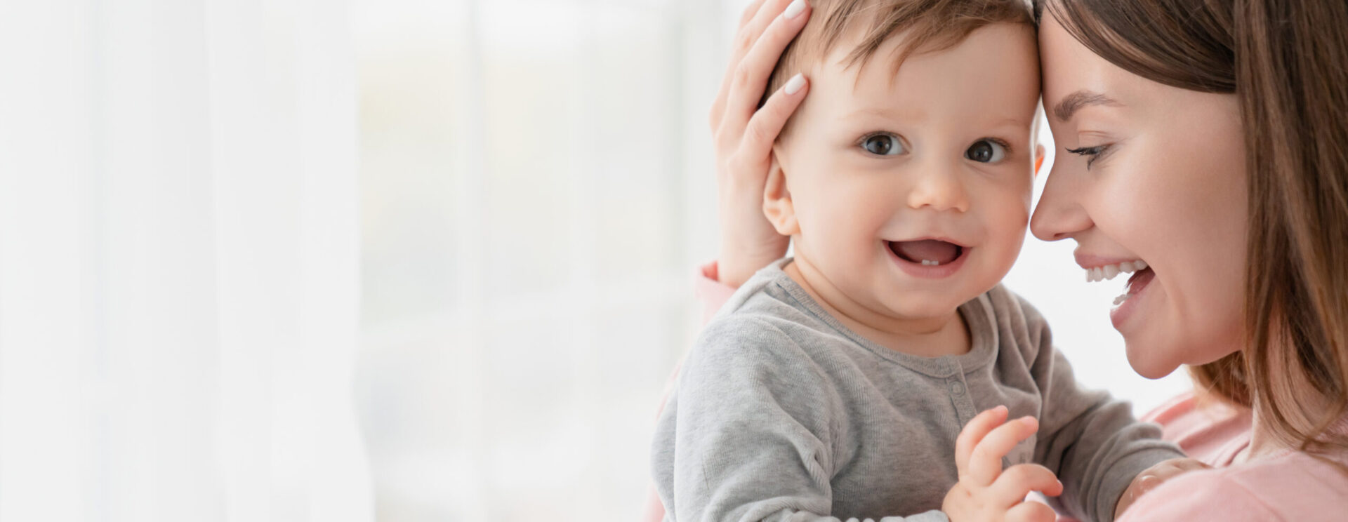 jeune femme brune aux cheveux longs qui porte dans ses bras un bébé de 6 mois environ très souriant.