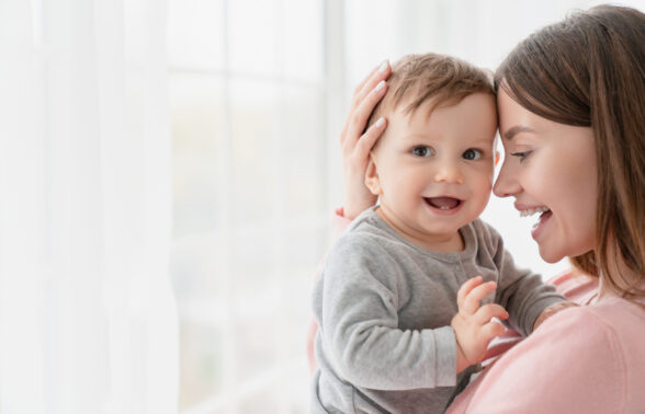 jeune femme brune aux cheveux longs qui porte dans ses bras un bébé de 6 mois environ très souriant.