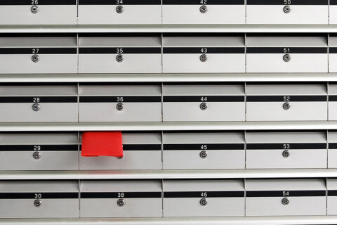 Série de boîtes aux lettres grises alignées avec une enveloppe rouge qui dépasse de l'une d'entre elles.