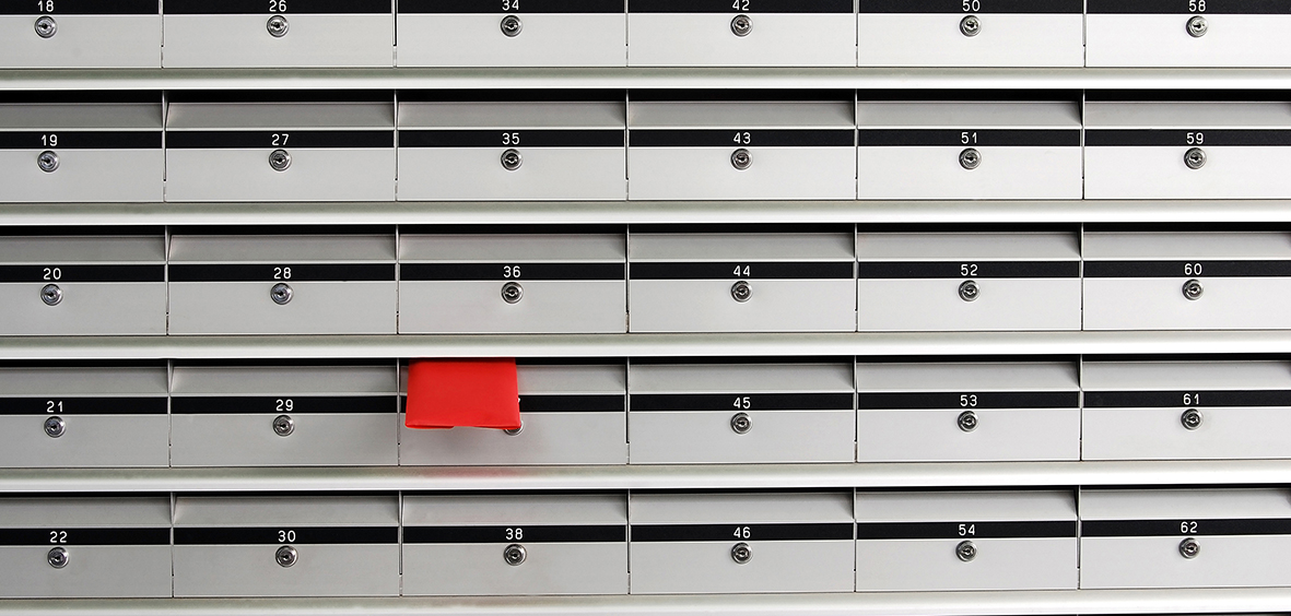 Série de boîtes aux lettres grises alignées avec une enveloppe rouge qui dépasse de l'une d'entre elles.
