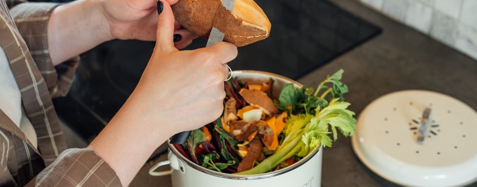 femme épluchant des légumes dans une cuisine et mettant les épluchures dans un composteur