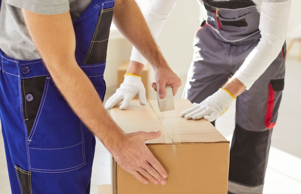 2 hommes en train de scotcher un carton de déménagement