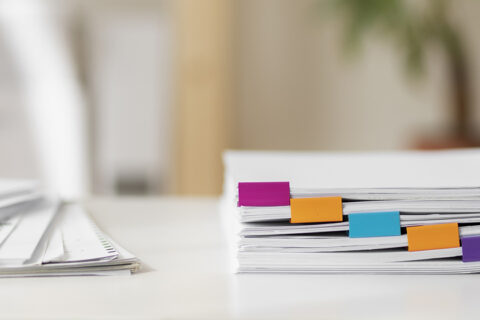 Feuilles blanches empilées sur une table avec des marque-pages violet rose et orange
