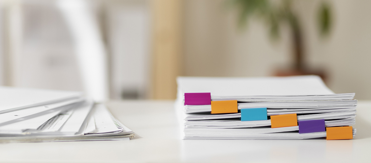 documents posés sur une table avec des marques-pages rose, orange et violet.