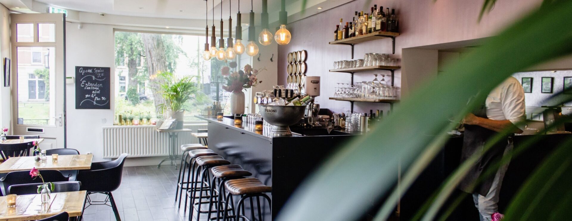 intérieur d'un café-restaurant. Ambiance vintage et cosy avec des meubles noirs et en bois, et une décoration soignée (bibelots en verre, bougies et panneau enardoise)