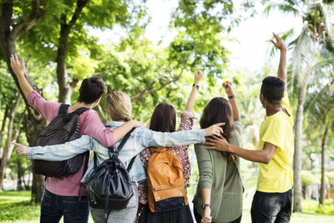 jeunes pris de dos dans une forêt. Ils se tiennent par les épaules et lèvent tous un bras.