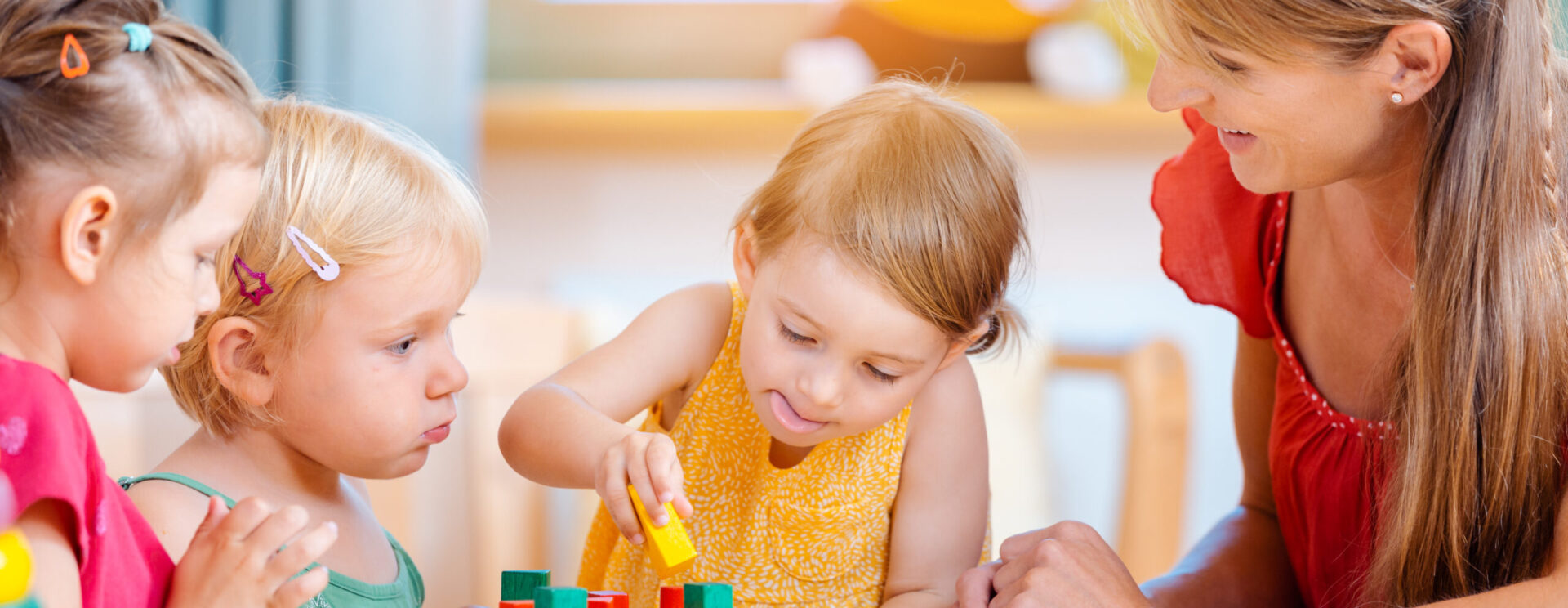 3 petites filles jouant à des jeux de bois avec une femme les surveillant
