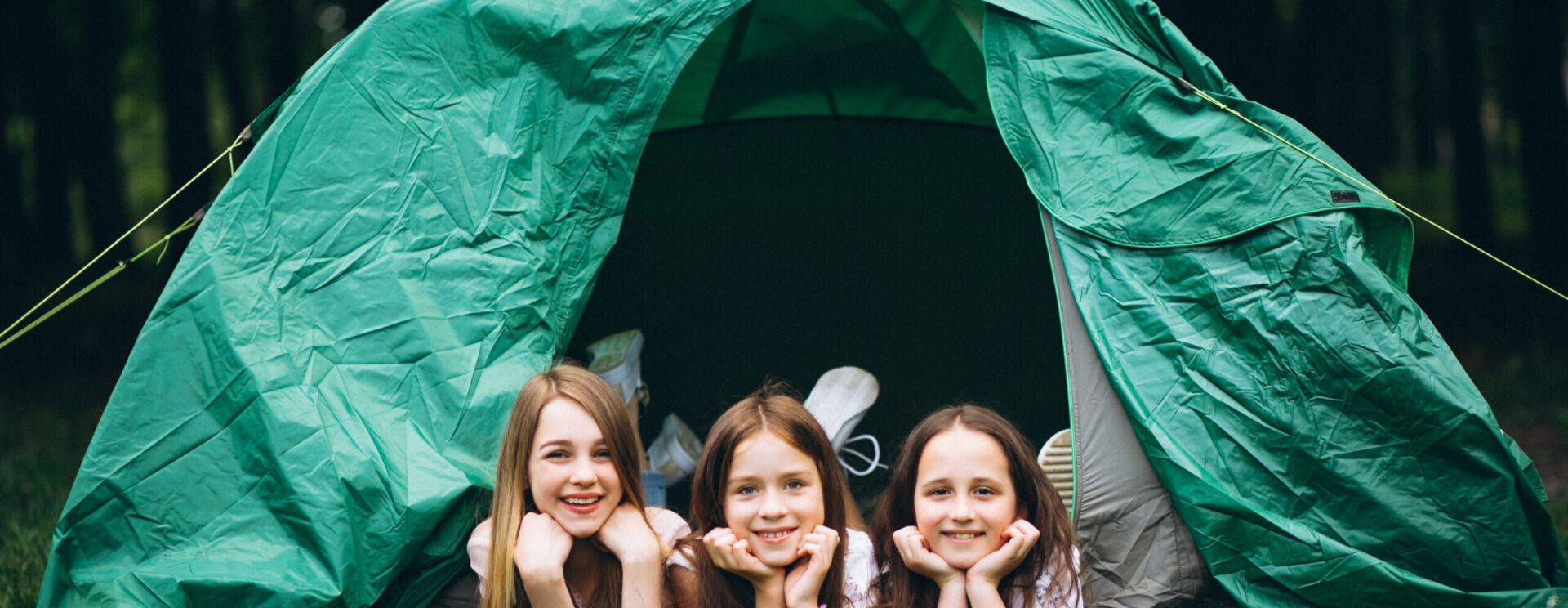 3 jeunes filles posant allongées à plat ventre devant une tente de camping verte