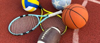matériel de sport : ballons de football, de handball et de rugby, ainsi que raquettes de tennis posés sur la surface d'un terrain de sport