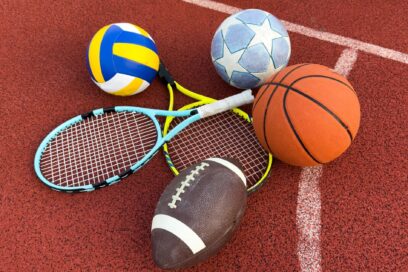matériel de sport : ballons de football, de handball et de rugby, ainsi que raquettes de tennis posés sur la surface d'un terrain de sport - Agrandir l'image, fenêtre modale