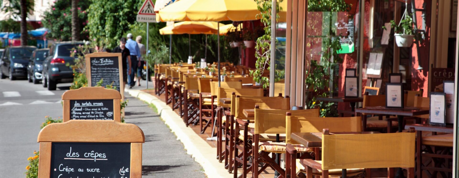 terrasse ensoleillée devant un restaurant. Chaises en bois avec dossier en toile jaune.