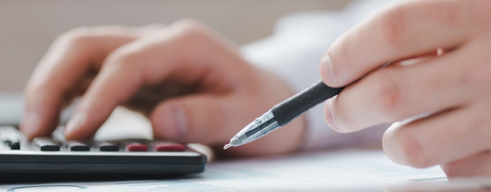 gros plan sur des maions tenant un stylo et appuyant sur les touches d'une calculatrice