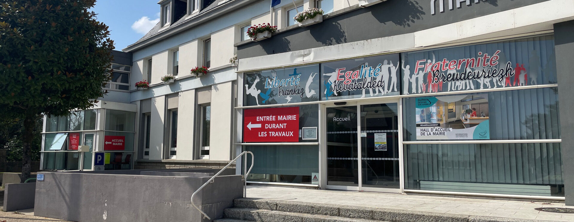 façade de la mairie de guipavas. Bâtiment de type années 1970-1980 avec une grande baie vitrée en façade. L''entrée est surplombée de 3 drapeaux : le drapeau français, le drapeau européen et le drapeau breton.