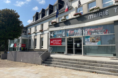 façade de la mairie de guipavas. Bâtiment de type années 1970-1980 avec une grande baie vitrée en façade. L''entrée est surplombée de 3 drapeaux : le drapeau français, le drapeau européen et le drapeau breton. - Agrandir l'image, fenêtre modale