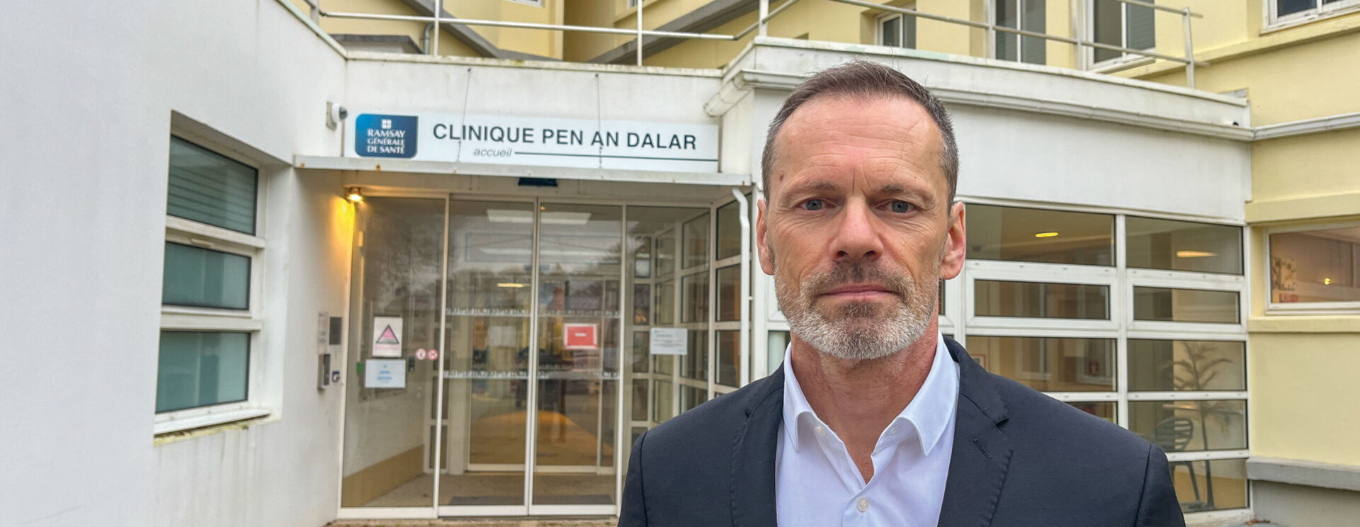 Portrait d'un homme brun, barbe courte grisonnante, devant la clinique Penn ar Dalar de Guipavas, dédiée à la santé mentale.