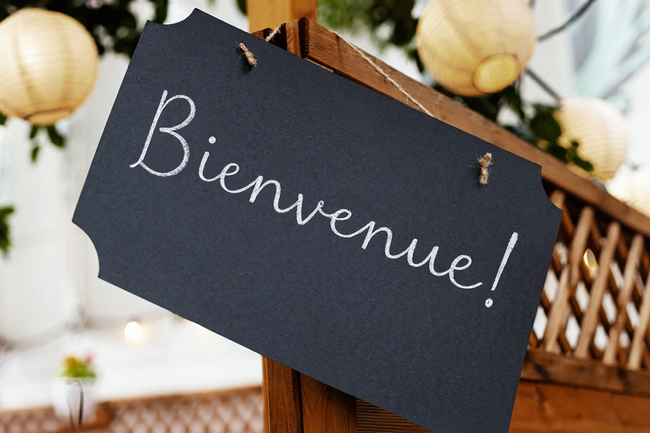 Ardoise accrochée à une barrière en bois. Sur cette ardoise il est inscrit "bienvenue".