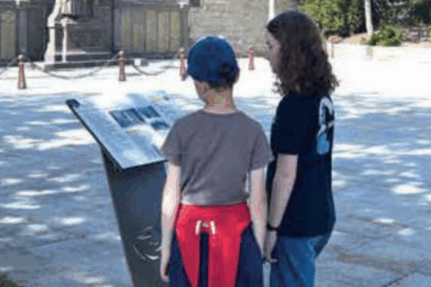 2 enfants face à la chapelle Notre-Dame-du-Reun à Guipavas. Ils lisent un panneau d'information sur ce monument. Ce panneau a été conçu dans le cadre du parcours de valorisation du patrimoine de la ville de Guipavas.