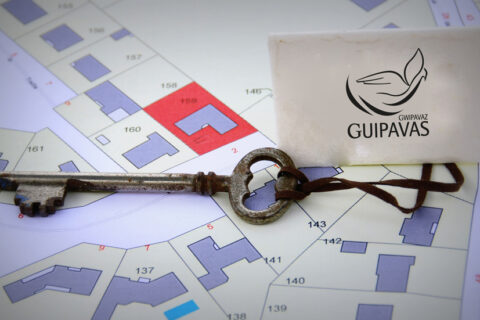 Clé ancienne à laquelle est attachée une étiquette avec le logo de la ville de Guipavas. En arrière-plan, un plan cadastral sur fond blanc.
