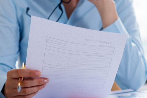 Zoom sur une femme portant une chemise bleue qui regarde une feuille de papier.