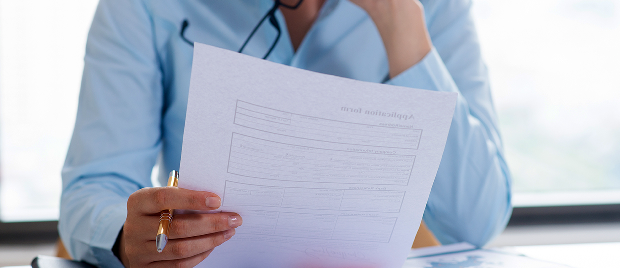 Zoom sur une femme portant une chemise bleue qui regarde une feuille de papier.