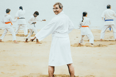 Homme en kimono blanc sur une plage. Dans le fond, plusieurs personnes également habillées en kimono blanc, en pleine démonstration de judo. - Agrandir l'image, fenêtre modale