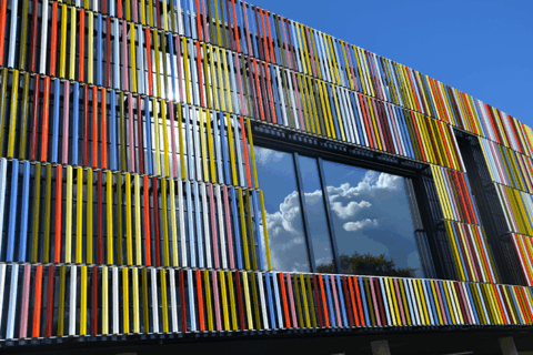 façade de la médiathèque de guipavas : une façade très colorée. Des bâtons de différentes couleurs sont alignés verticalement pour recouvrir l'entièreté de la façade. Le ciel bleu se reflète sur la grande fenêtre qui complète l'ensemble.