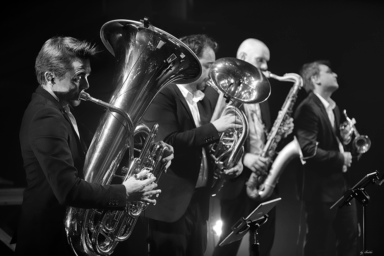4 musiciens qui jouent sur scène du trombone, du saxophone et de la trompette. Photo en noir et blanc.