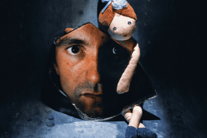 image issue du spectacle Eurydice. Visage d'un homme en gros plan qui semble entouré de métal et sur lequel est accroché une poupée de chiffon. - Agrandir l'image, fenêtre modale