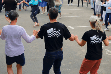 hommes et femmes qui dansent une danse bretonne en extérieur. Certains portent le drapeau breton sur leur tee-shirt. ils 'agit d'une scène prise lors de la fête de la Bretagne à Guipavas.