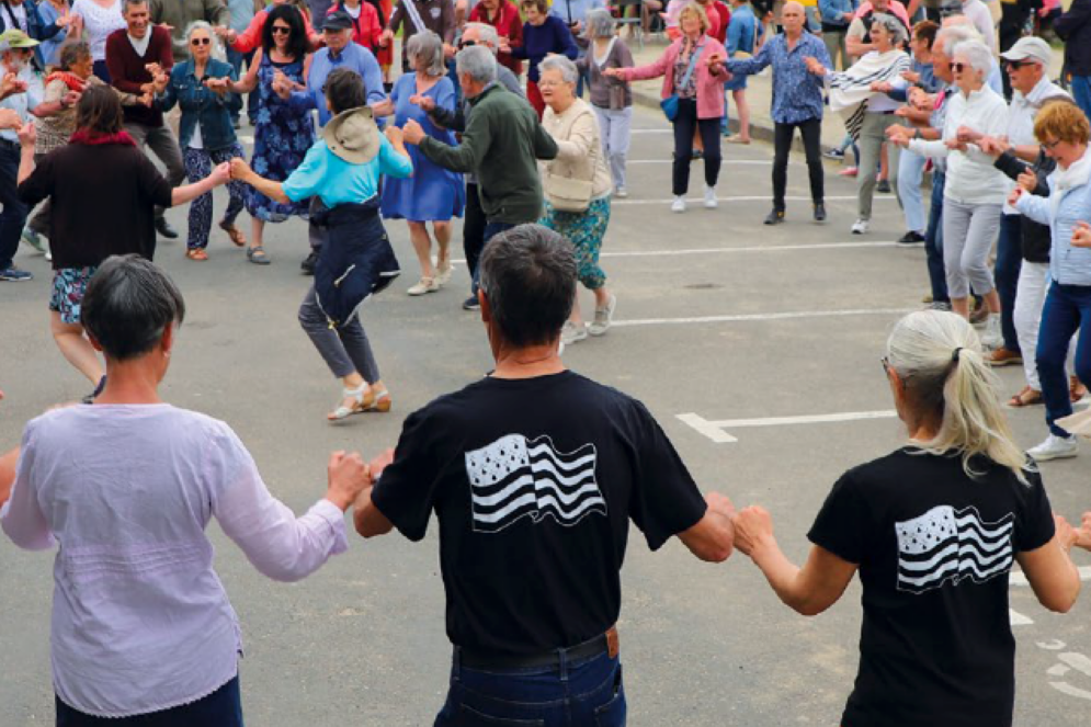 hommes et femmes qui dansent une danse bretonne en extérieur. Certains portent le drapeau breton sur leur tee-shirt. ils 'agit d'une scène prise lors de la fête de la Bretagne à Guipavas.