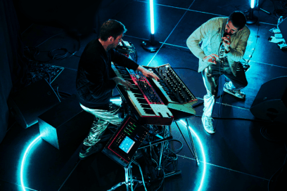 2 musiciens sur scène. Le groupe Potsiikei. la scène est peu éclairée : cercle de néons bleutés au sol, néon bleuté derrière les artistes. L'un des musicien tient un micro. L'autre joue sur un piano numérique. - Agrandir l'image, fenêtre modale