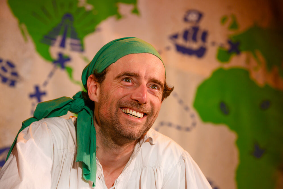 photo portrait d'un homme souriant habillé en pirate devant une carte aux trésors