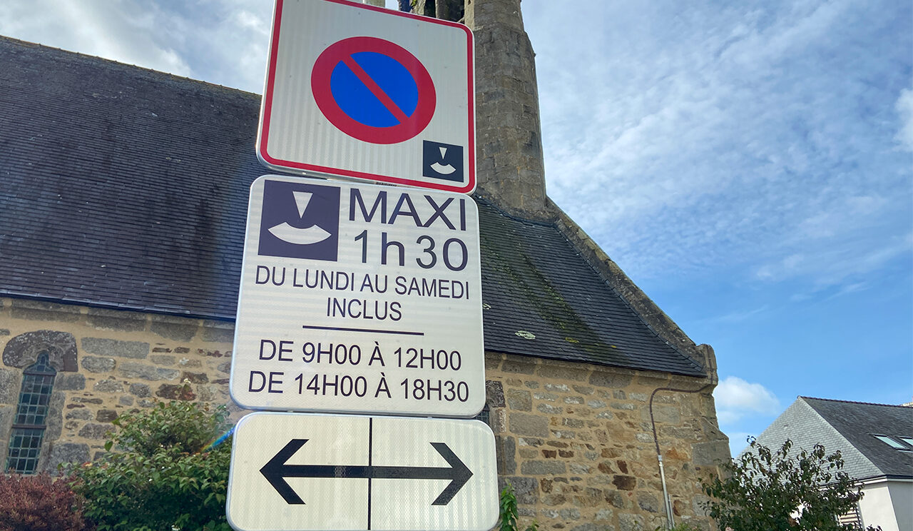 panneau de signalisation expliquant que le stationnement en zone bleue est limité à 1h30 maxi, du lundi au samedi inclus, de 9h à 12h et de 14h à 18h30. Le panneau est positionné à proximité de la chapelle Notre-Dame du Reun au centre-ville