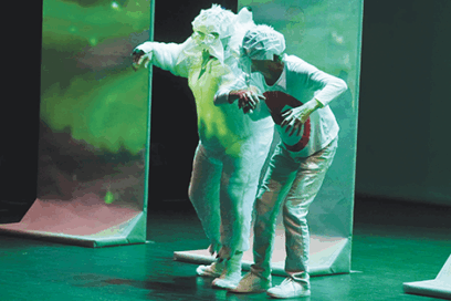 photo du spectacle Ressorts : ambiance sombre, éclairage vert. Deux personnes sur scène habillée en blanc, ou plutôt déguisée. L'un eporte un masque chirurgical et une charlotte. L'autre est recouvert de papier blanc, tel un monstre ou une créature fantastique. - Agrandir l'image, fenêtre modale