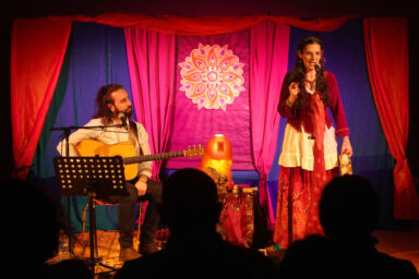 Un homme guitare à la main et une femme devant un micro en train de donner un spectacle de conte