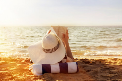 une femme de dos portant un grand chapeau blanc lisant un livre allongée sur une place, au soleil couchant devant la mer - Agrandir l'image, fenêtre modale