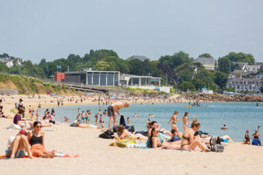 Vue d'estivants sur la plage du moulin Blanc. Certains sont sur leurs serviettes, d'autres se baignent